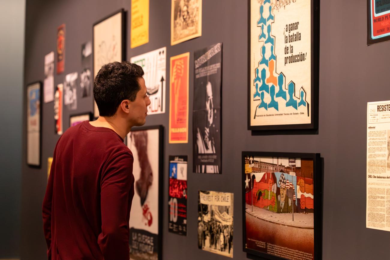 A man looks at a gallery of artwork featuring posters from 1973 coup