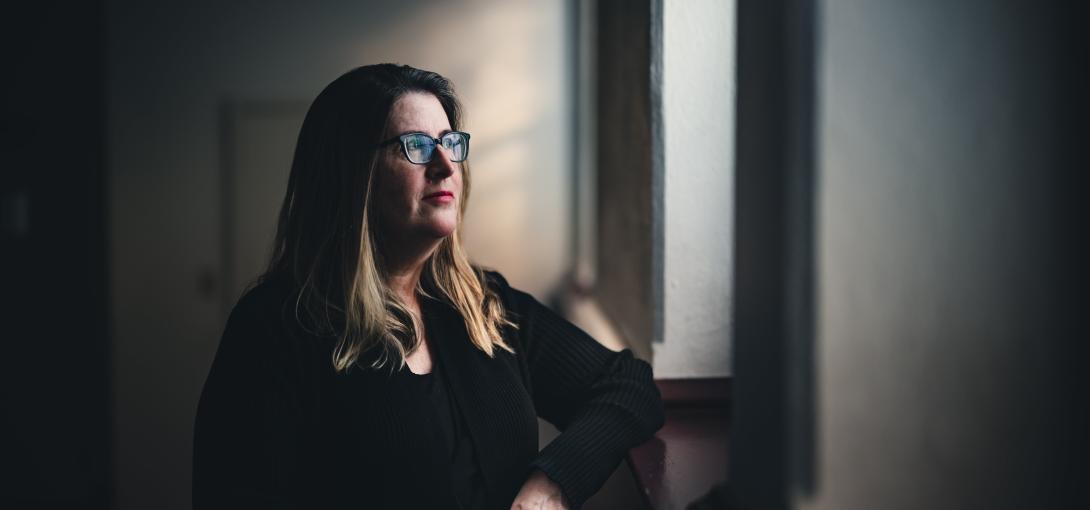 Monica Najar stands near a window and looks stoically towards the light.